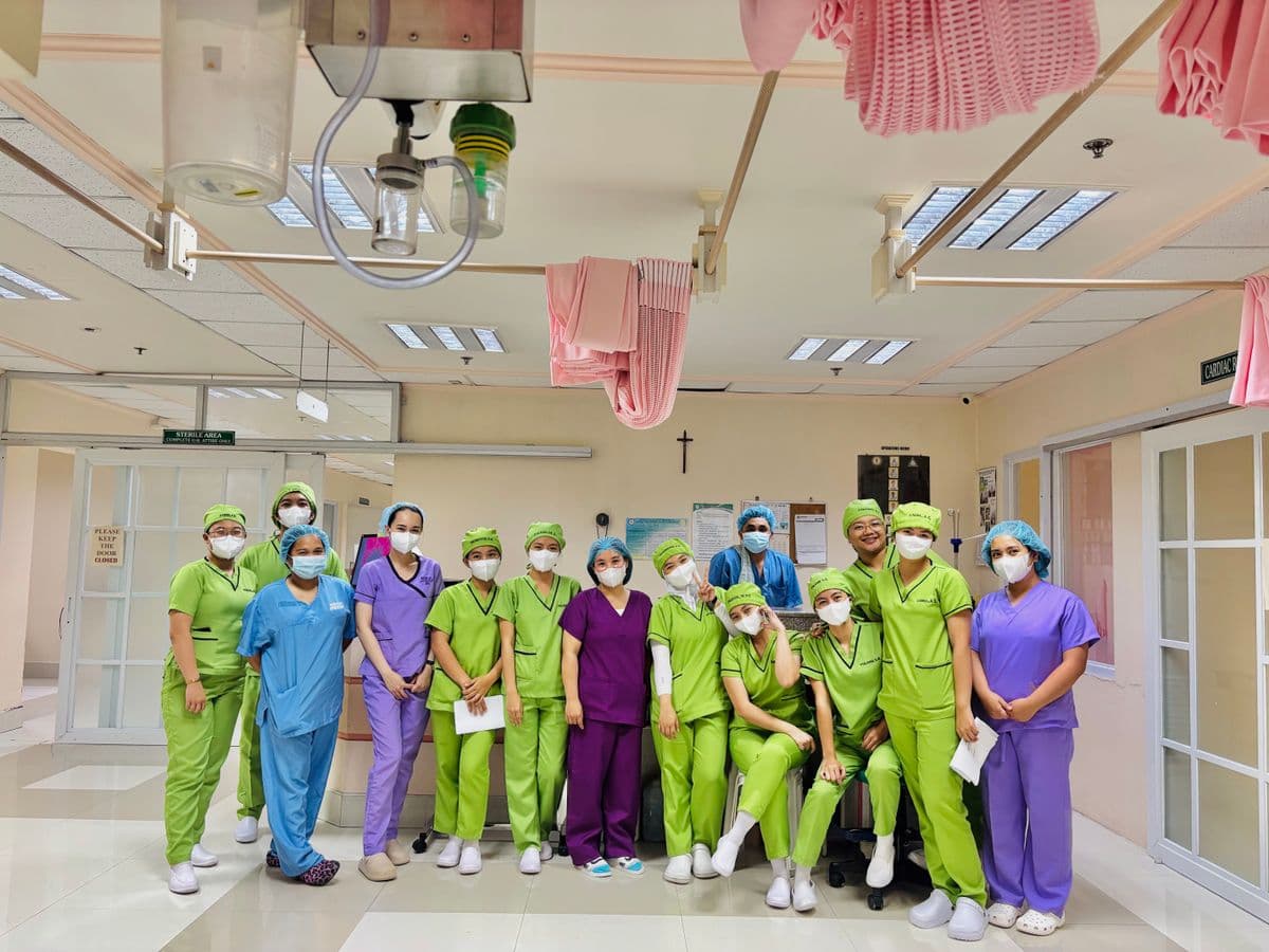 Group of nurses in colourful scrubs and face masks standing together in a hospital ward