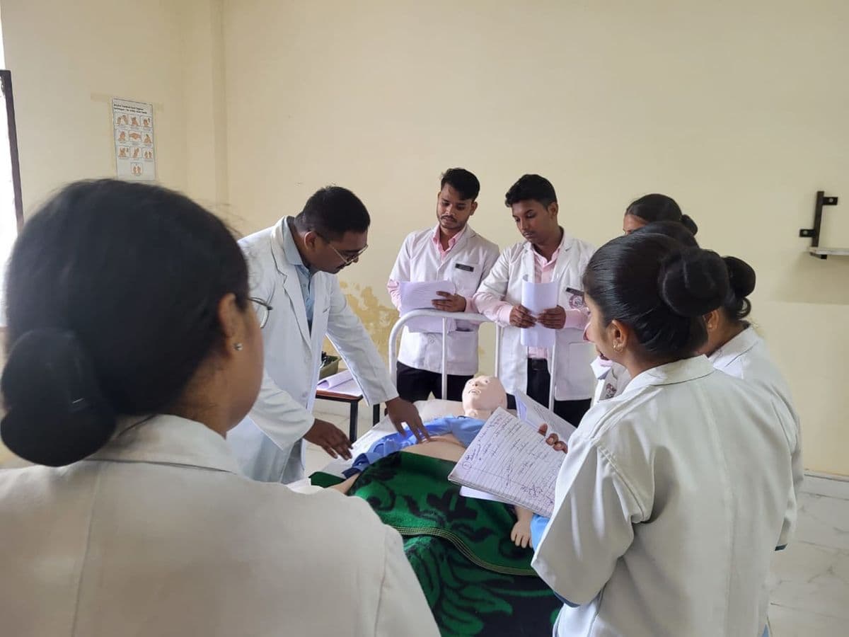 Nursing students in white coats practise on a manikin with their instructor in a skills lab