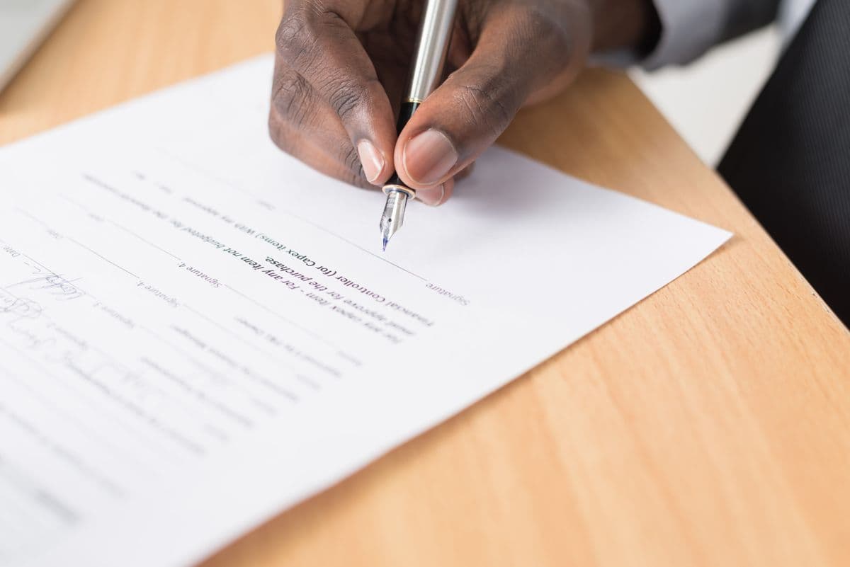 Hand signing a printed contract with a fountain pen on a wooden desk