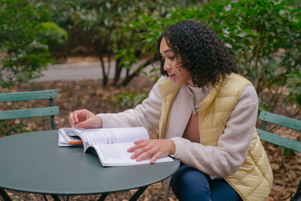 Young woman reading a textbook at an outdoor table