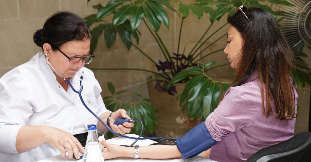 Mature nurse in a white uniform measuring a young woman's blood pressure at a table