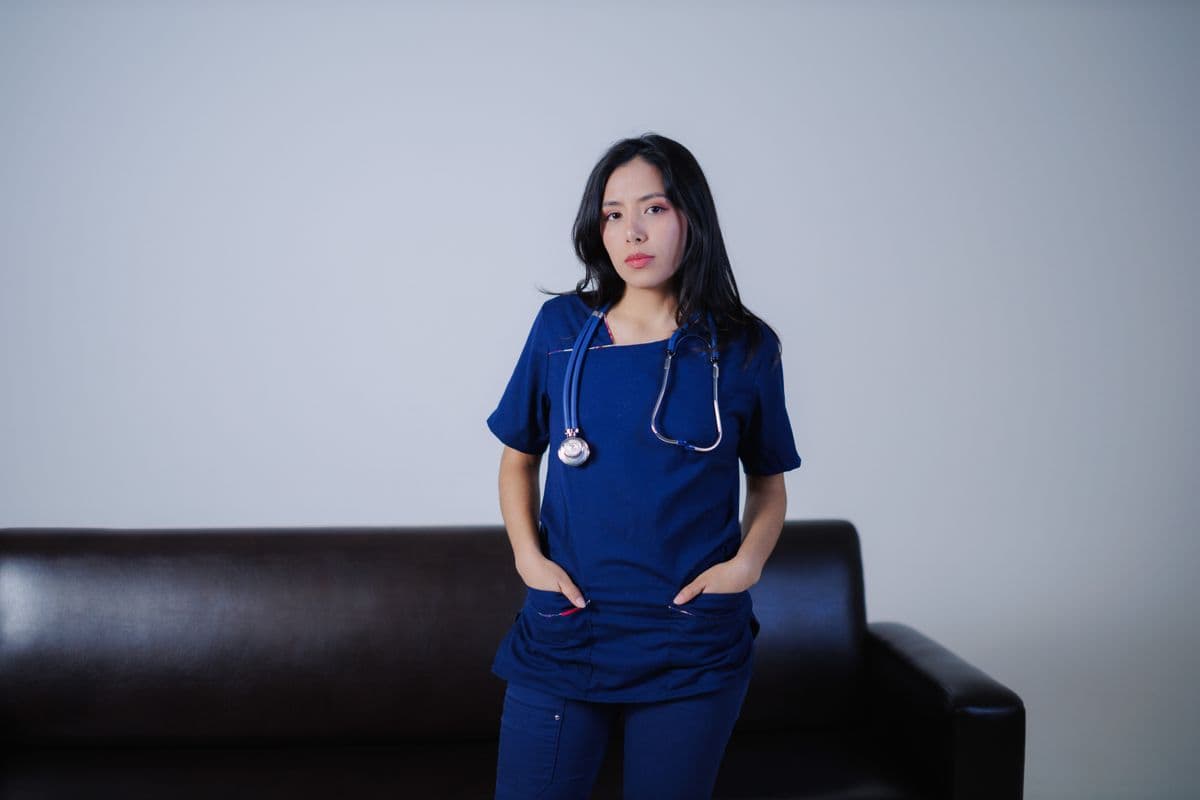 Young nurse in navy scrubs with a stethoscope standing in a hospital room